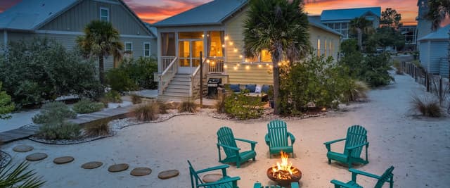 Beachfront vacation home at sunset with lit fire pit and green Adirondack chairs on sand