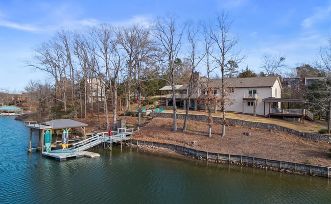 Waterfront property with white house, boat dock, and bare trees along calm lake or river